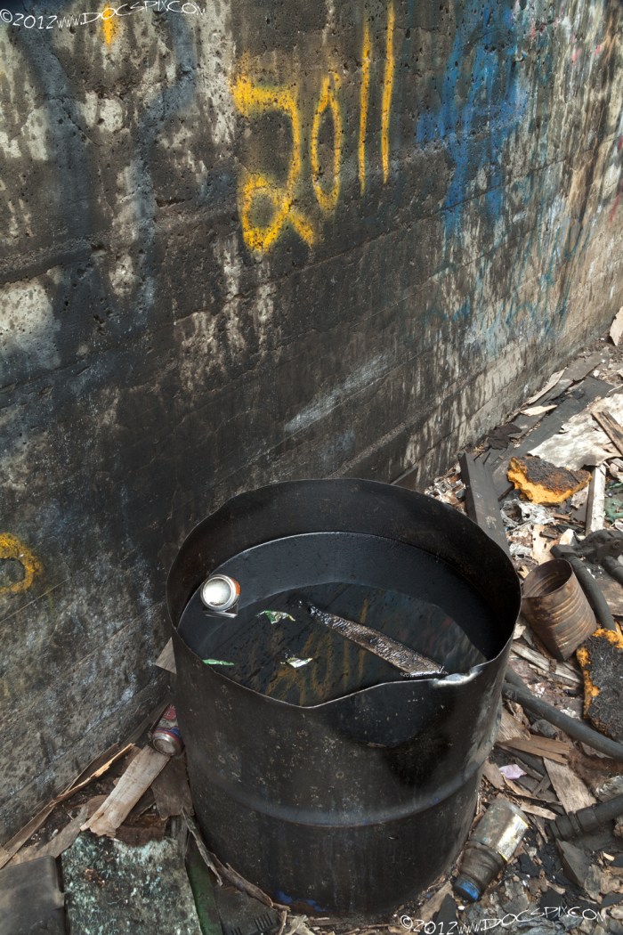 A half-oil drum sits next to the north wall of the factory floor. 