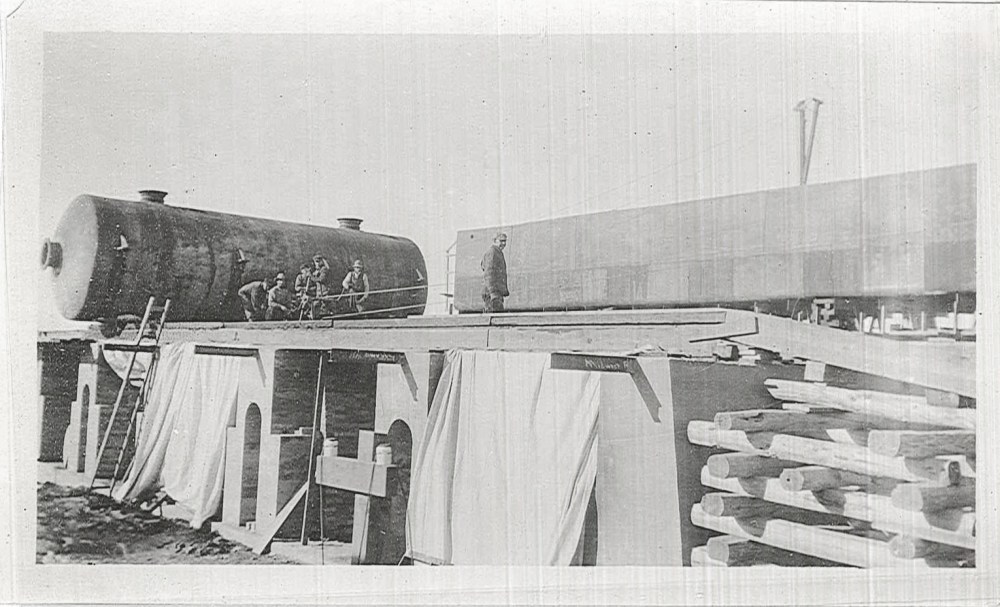 A still tank rests on temporary rails atop the foundations.