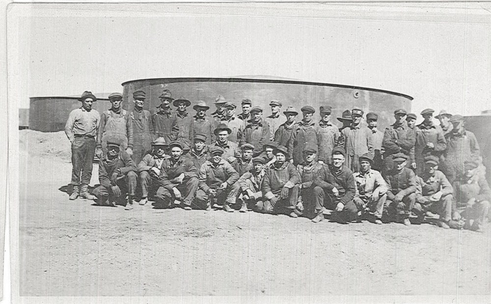 A group of men pose for a photograph in front of one of the storage tanks. 
