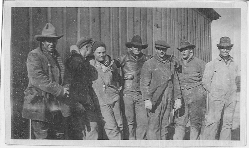 A group of men pose for the camera near one of the temporary buildings. 