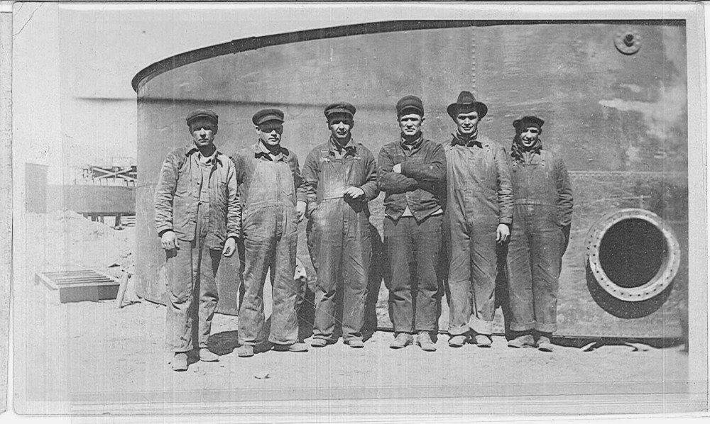 A group of men stand in front of a storage tank. 