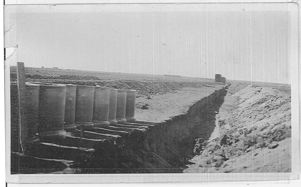 Pipes are laid out next to a trench. Note the rail cars in the distance and the rail line that was placed for the delivery of equipment. 